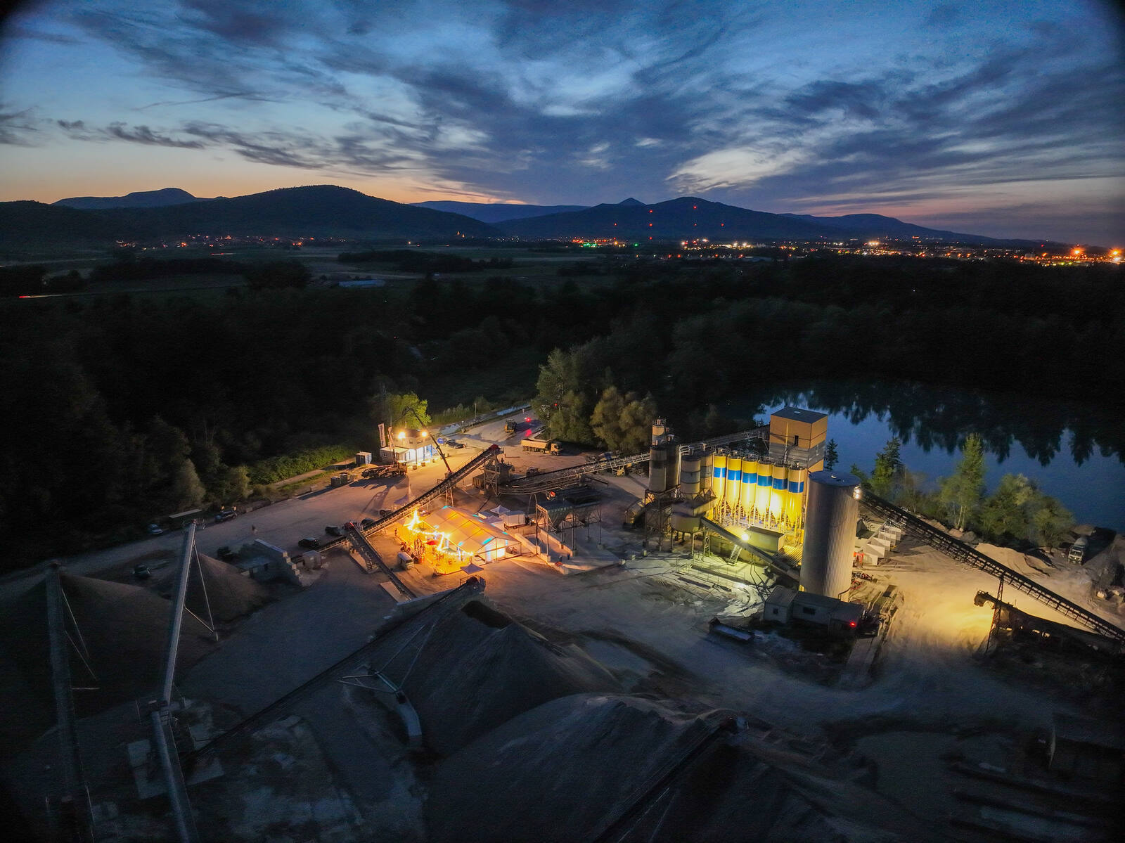 Vue aérienne au crépuscule : chapiteau illuminé au milieu d'un site de production de granulats, lors d'une journée portes ouvertes industrielles