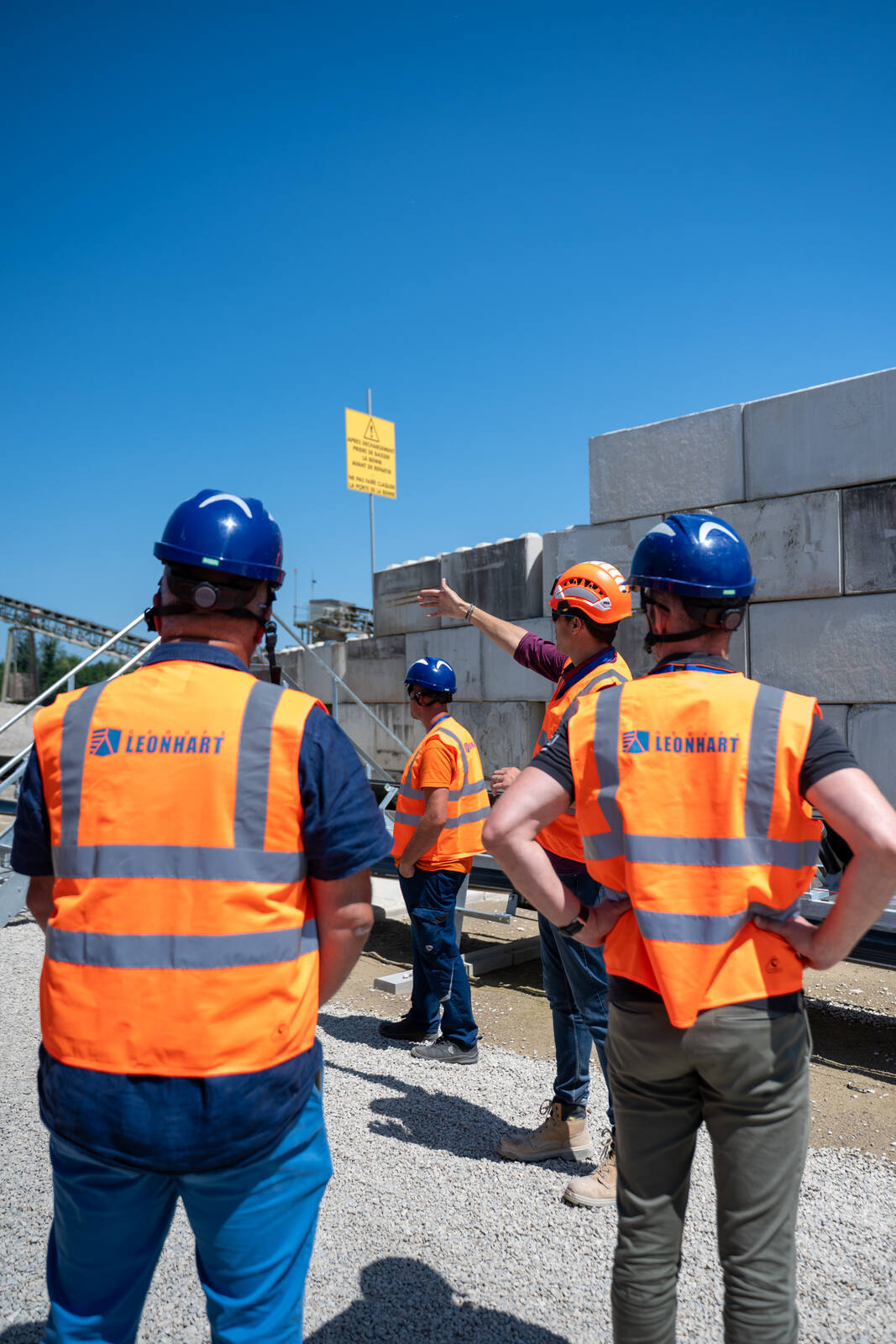 Visiteurs en gilet devant des blocs de béton empilés, explication en cours